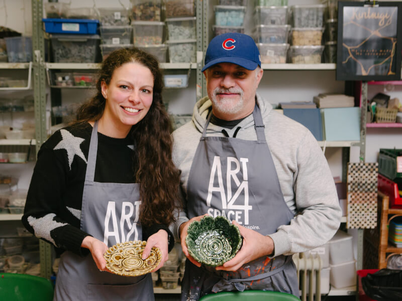 A man and woman are standing up, holding two coil clay bowls that have been fired and glazed